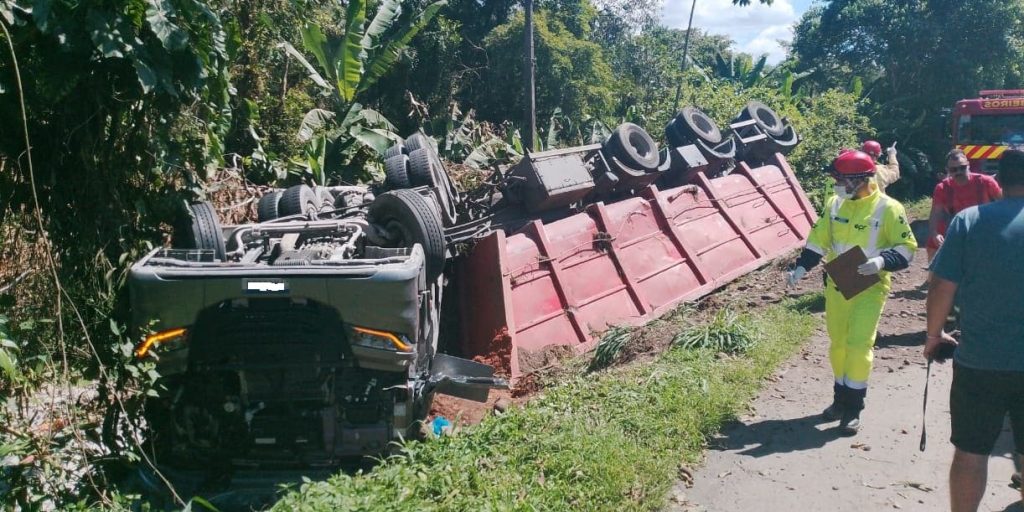 Vítima é retirada de caminhão por outros motoristas, após tombamento